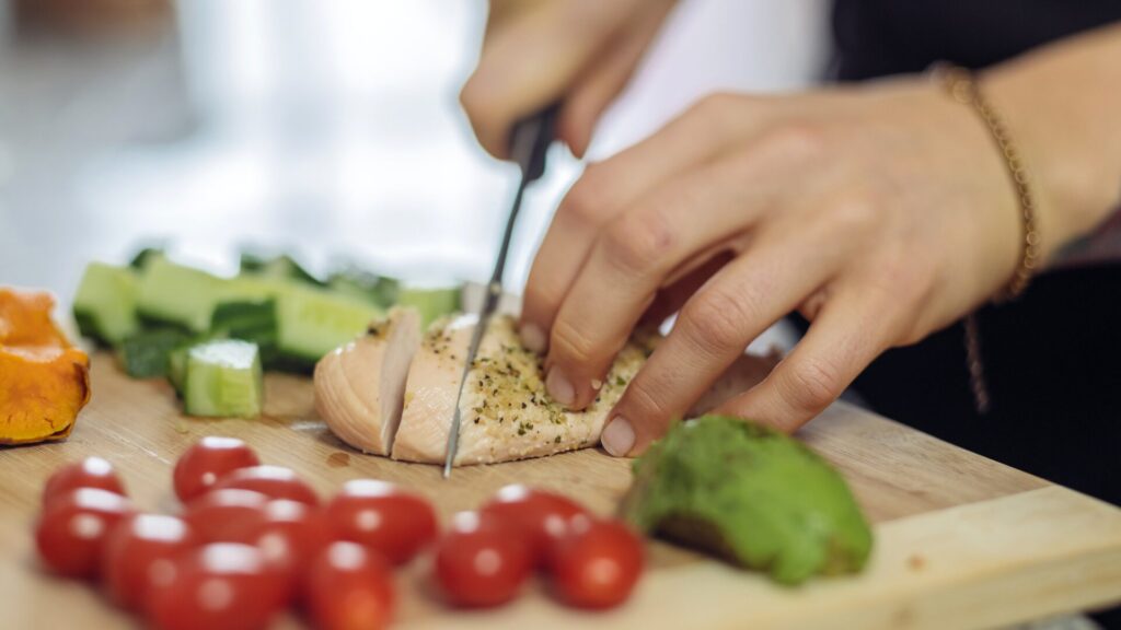 Mains coupant un filet de poulet frais sur une planche de découpe entourée d’aliments sains, illustrant les conseils nutritionnels LaserAddict pour éviter la rechute après l’arrêt du tabac.