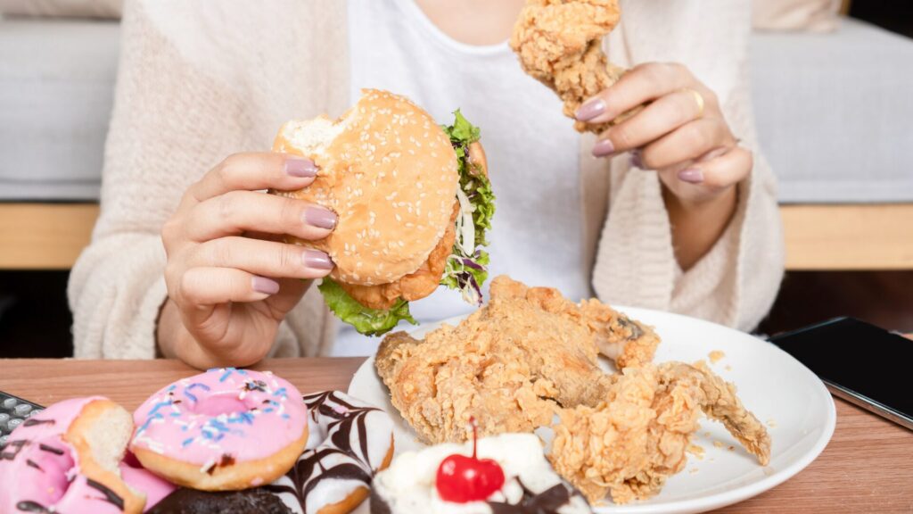 Femme mangeant de manière compulsive un mélange d’aliments sucrés et salés, illustrant les troubles du comportement alimentaire et la dépendance émotionnelle à la nourriture.