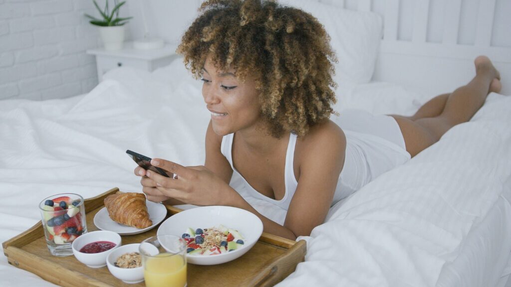 Femme au réveil dans son lit savourant un petit-déjeuner équilibré, symbolisant l’importance du sommeil et de la nutrition après un sevrage – LaserAddict