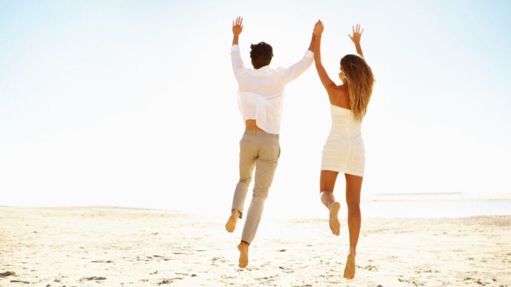 Couple courant sur la plage en vêtements clairs et légers, illustrant une préparation du body summer saine et équilibrée avec LaserAddict