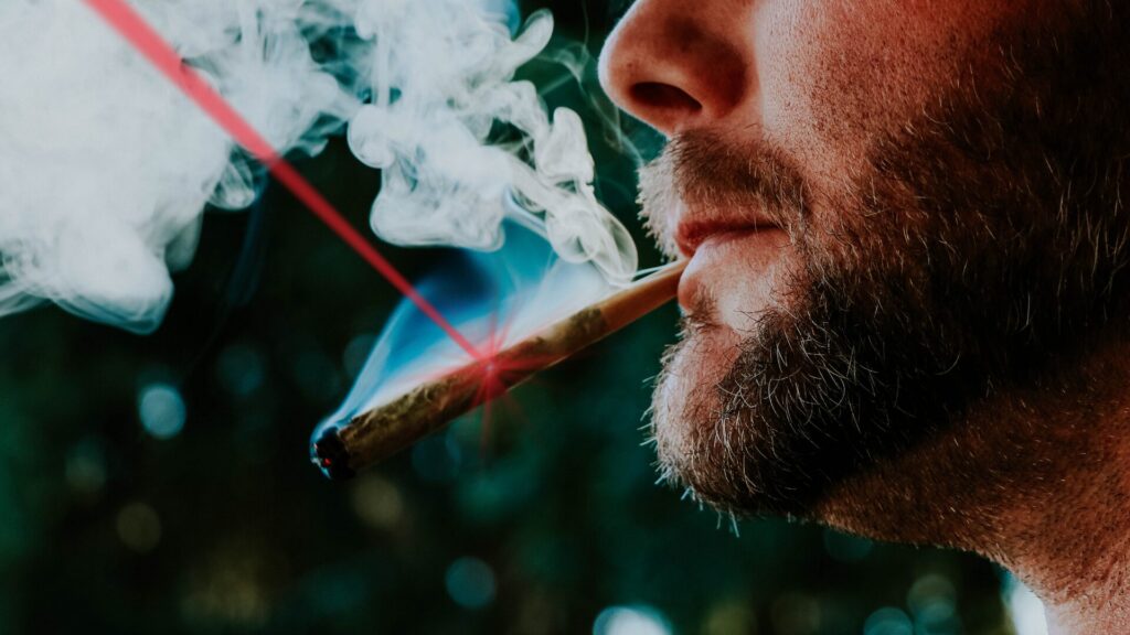 Fumeur tenant un joint à la bouche, avec un faisceau lumineux rouge symbolisant le laser de la méthode LaserAddict pour l’accompagnement au sevrage du cannabis.