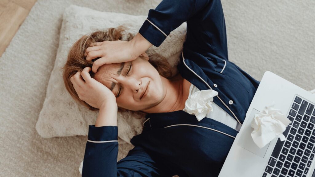 Femme stressée dans son lit avec un ordinateur portable, se tenant la tête entre les mains, illustrant les troubles du sommeil liés au stress accompagnés par LaserAddict